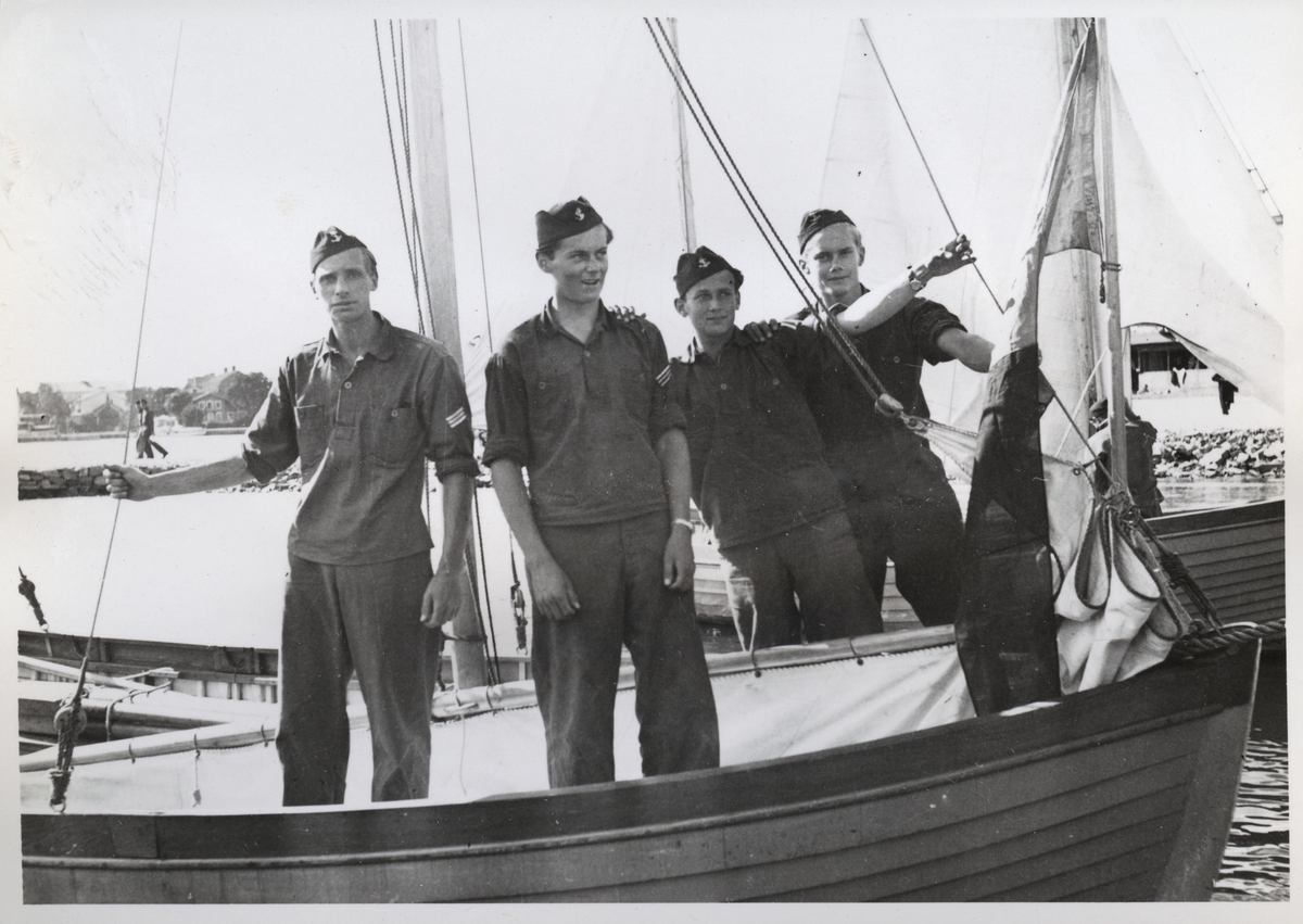 Porträtt av fyra värnpliktiga som står i en mindre segelbåt