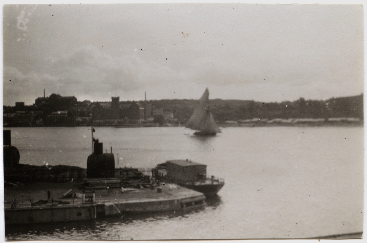 Vy över Saltsjön från Beckholmen, 1920-tal. I förgrunden del av docka på Beckholmsvarvet med förtöjd arbetsbåt, på sjön segelskuta. T v i bakgrunden Danvikshemmet och Saltsjö kvarn.