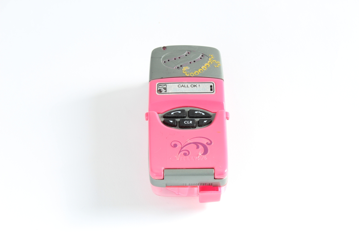 Tilhørt jente (f. 2001) i Sør-Odal. 
En rosa mobiltelefon-leke. Den er utformet som en normal mobil i størrelse. Med trykkbare taster og lokk til å åpne. Den er dekorert med en gul sommerfugl.