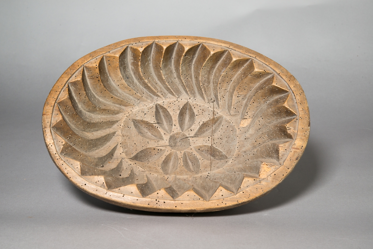 Grötform, oval, av trä, enligt äldre kataloglapp av al. Invändigt i mitten utskuren blomma med mera i djup relief. Utsidan slät.