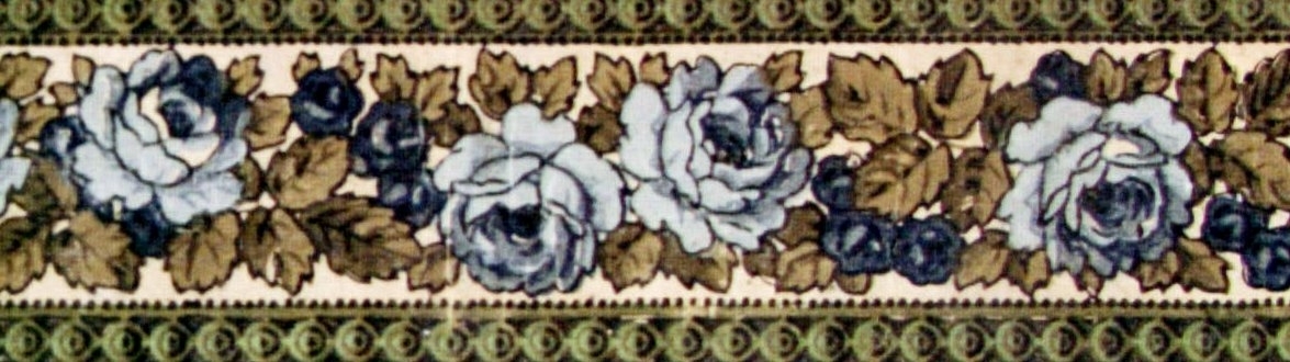 Rosenranka i tre ljusblå nyanser med blad i beige och grått på en cremevit bakgrund. Bården avslutas upp-/nedtill med band dekorerade med cirklar och små prickar i två grågröna nyanser.