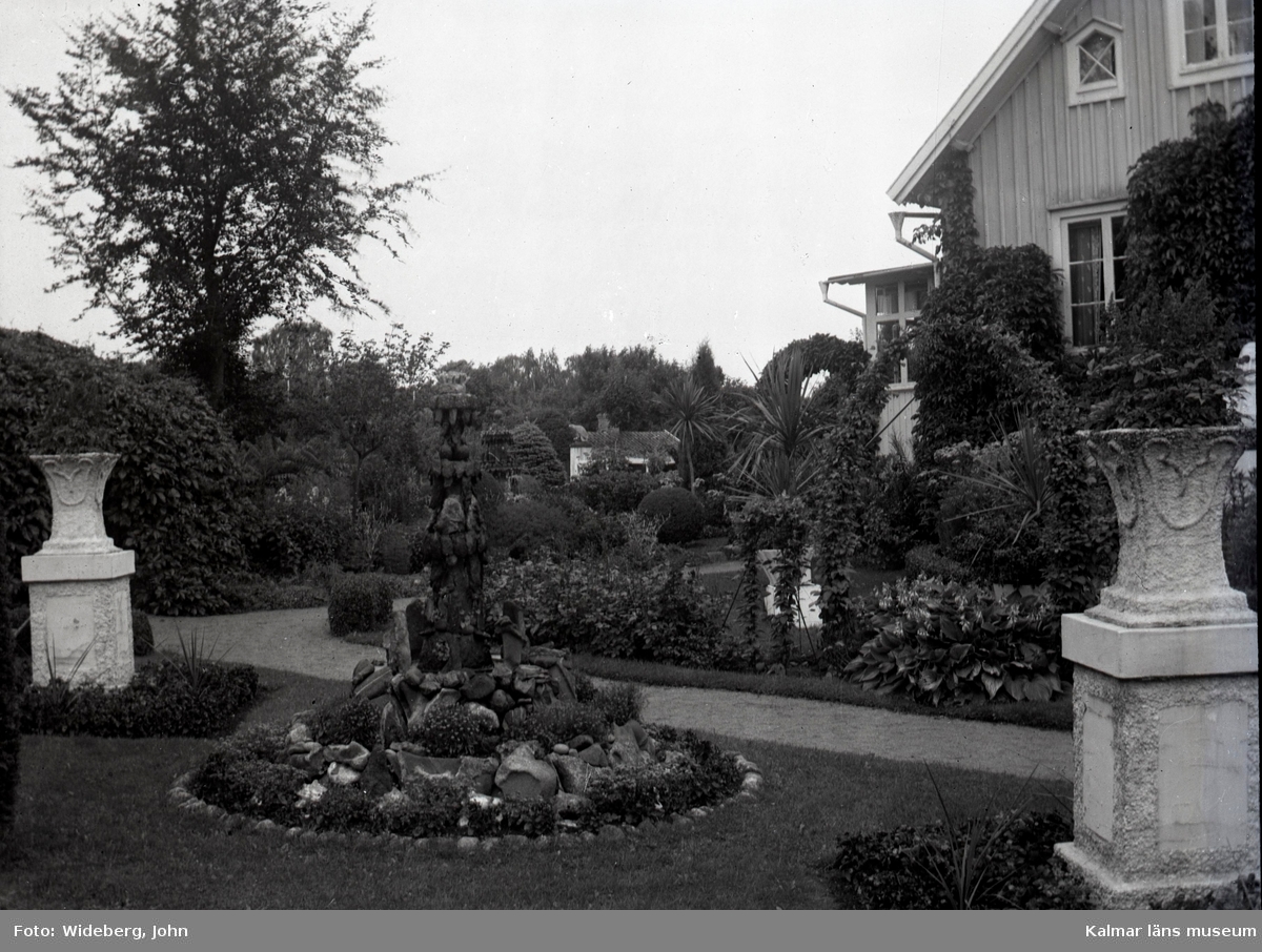 Västra gaveln av huset i Widebergs trädgård.

John Wideberg blev tidigt intresserad av
trädgårdsanläggningar. Han hade sannolikt hämtat
inspiration på resor han gjort till Stockholmsutställningen
1897 och till Göteborg 1923. Han blev också vän med
stadsträdgårdsmästaren Haglund i Kalmar.
John hade palmer i potatiskällaren under huset och påfåglar,
ekorrar och pärlhöns som övervintrade i hönshuset. En
papegoja och en sköldpadda fick tillbringa vintrarna inne i
köket. Runt trädgården planterade han skyddande häckar.
Arbetet påbörjades redan när han var 18 år med att han
hämtade åtta granar i skogen, och planterade dem i en
ring mitt i trädgården. Dessa finns kvar än idag. I slutet
av 1930-talet arrenderades jordbruket ut och John kunde
ägna sig på heltid åt trädgården, som blev alltmer av ett
besöksmål. John började ta inträde, 25 öre.
John utvecklade också sin hobby som tavelmålare och som
fotograf. Han tog med sin lådkamera under årens lopp
hundratals vackra bilder från trädgården, liksom på vyer,
hus och människor i takten. Ca 500 av dessa bilder finns
bevarade som glasplåtar, skänkta till Kalmar läns museum.
