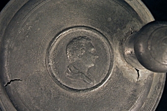 Dryckesstop av tenn med Carl XIV Johans bild på locket. Handtaget något skadat.