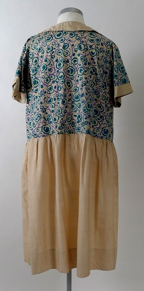 Klänning av chantung. Kjolen är sydd av ofärgad chantung. Överdelen i chantung har ett tryckt mönster i grönt och lila. Framtill på livet finns två fickor. Krage baktill. 1920-talet.