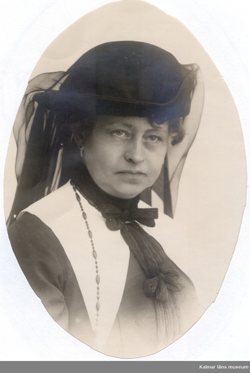 Ovalt foto av Ellen Warholm i stor, svart hatt med svart, långt flor bak och vit krage med midjelånga snibbar.
