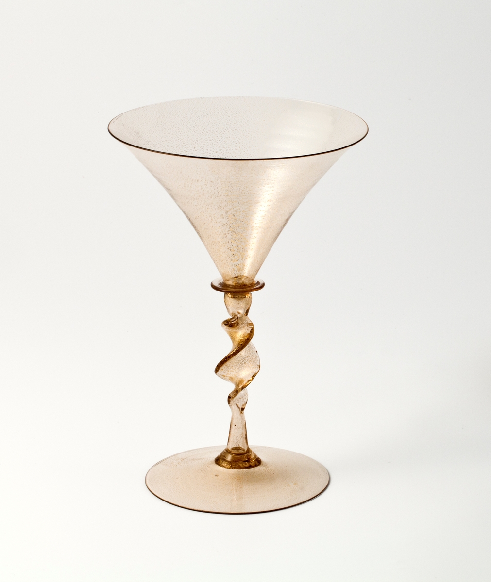 Glasspokal med konisk cupa, spiralformet stett og svakt hevet fotplate. Brunlig glass med innlagt bladgull.