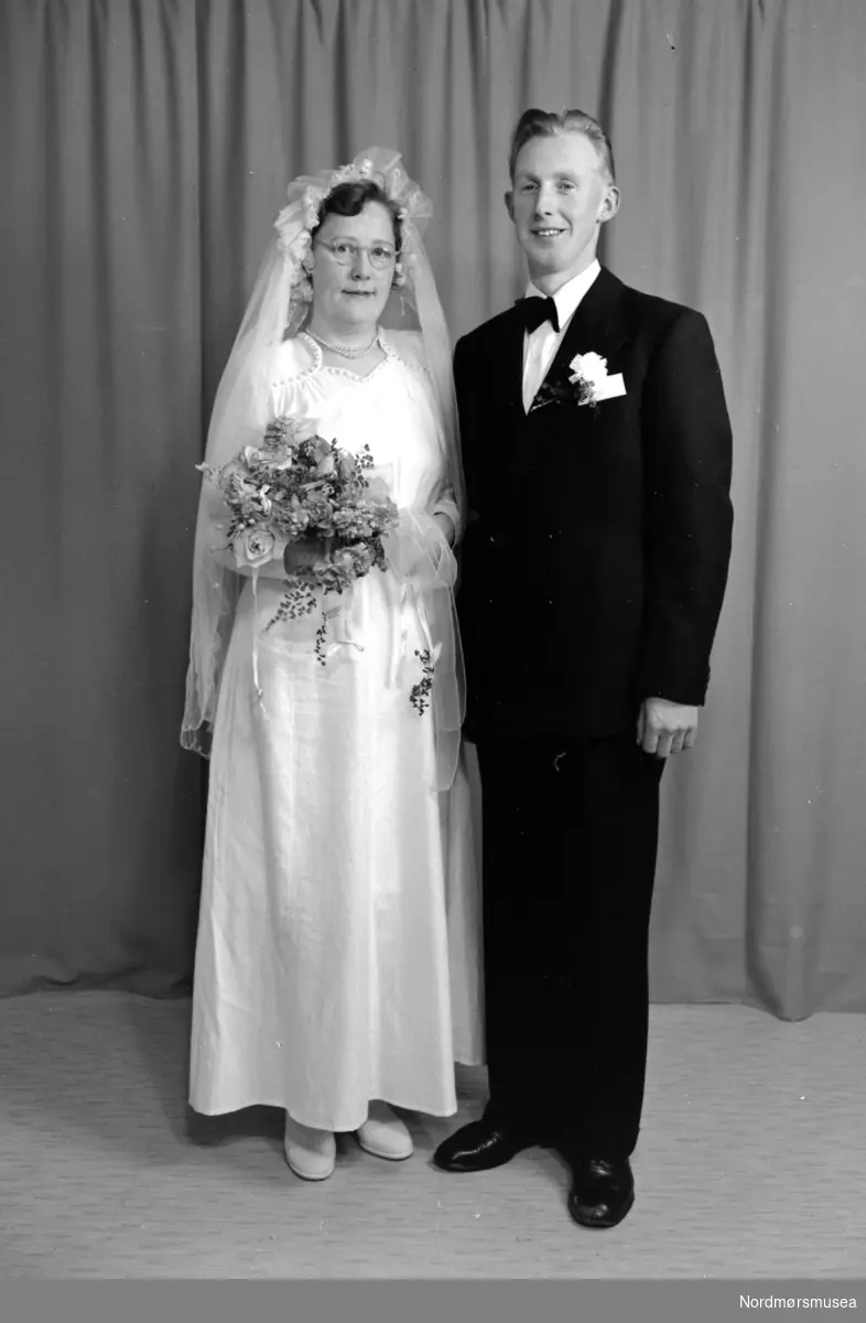 Foto av et brudepar. Paret er sannsynligvis fra Tingvoll kommune i Møre og Romsdal. Datering er omkring 1950-1960. Fra Nordmøre museums fotosamlinger, Halås-arkivet. Serie.
