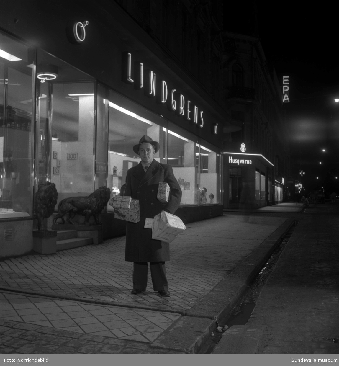 En man gör sina julklappsinköp på Lindgrens järnhandel. Exempel på julklappar: leksakståg, handarbete, ljuslykta och primuskök. Bilderna är tagna för ett reportage i tidningen Husmodern.