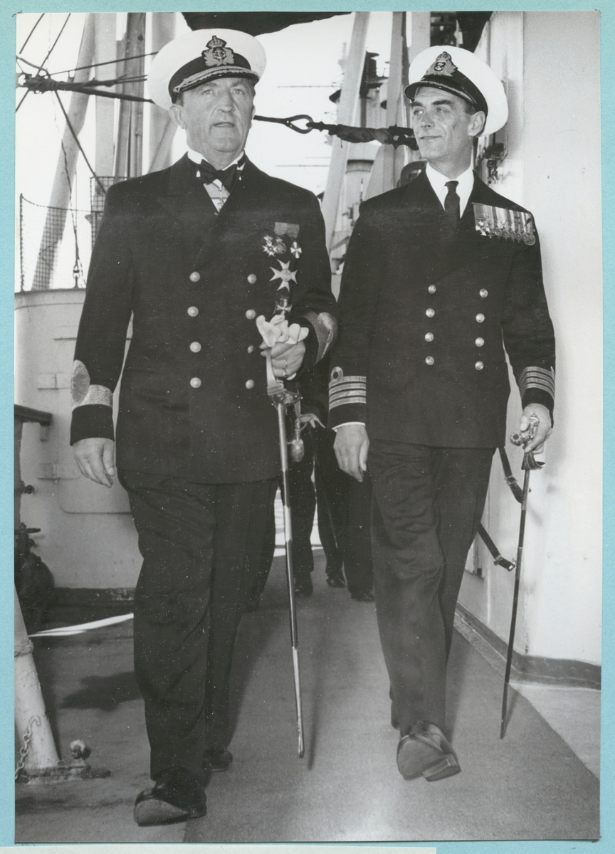 Konteramiral Samuelson på inspektion av fartyget H.M.S. Montclare i sällskap av fartygets chef Captain Hutchinson. Båda är klädda i uniform med medaljer på bröstet samt i mössa. I händerna håller de i varsin käpp. 
Från Engelska besöket i Karlskrona den 9-14 september 1951.