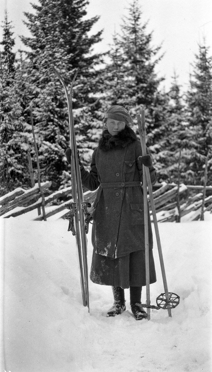 Uidentifisert kvinne med ski. Snøkledd skog i bakgrunnen.