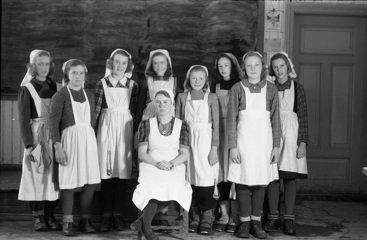 Sju bilder av jenter på "kokkeskole", trolig Hoffsvangen skole 1945. Foran sitter husstellærer Aslaug Glemmestad, senere gift Wedøe. Bak fra venstre (bilde nr. en): Edel Nettum, ukjent, Bjørg Kristiansen, Solveig Jensen, Kari Karsrud, Jorun Tørnby, Petra Stenbak, Jorun Løvstad (?).