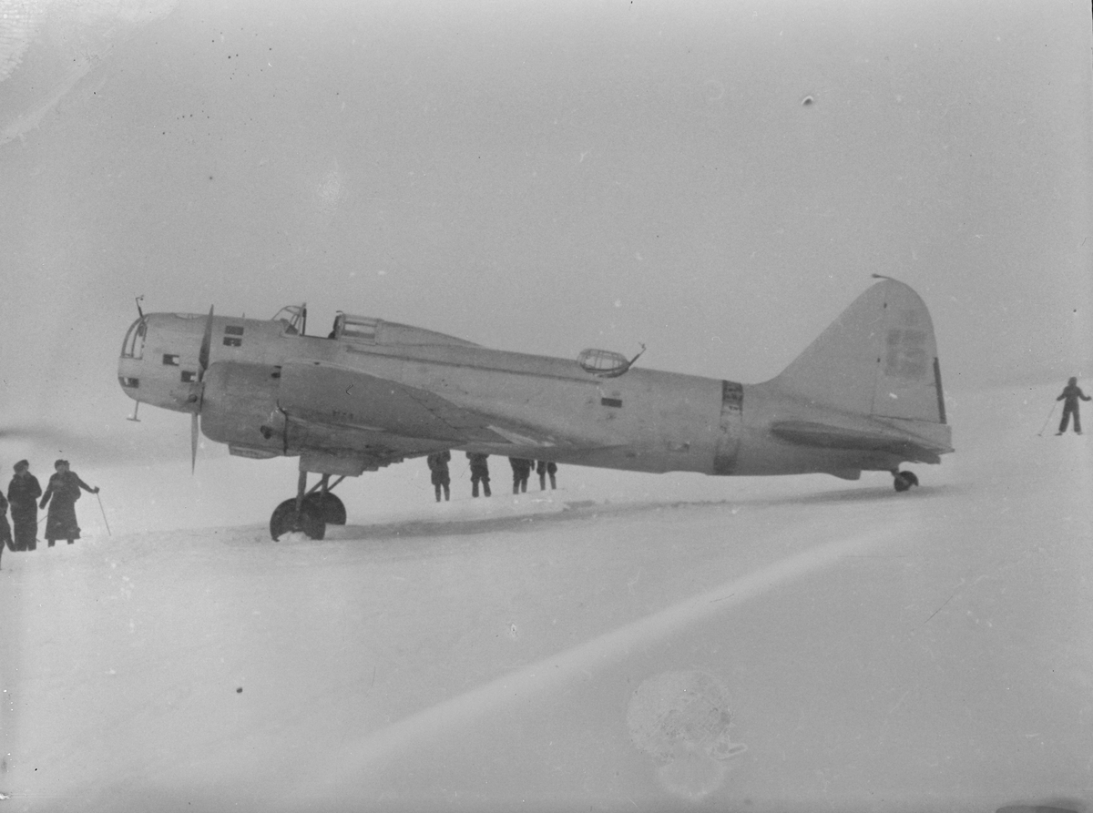 Sovjetiskt flygplan Iljushin DB-3 står på ett fält under finska vinterkriget, 1940. Människor i rörelse runtomkring. Bild från F 19, Svenska frivilligkåren i Finland.