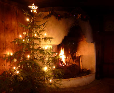 Et juletre med lys, juletrepynt og stjerne i toppen står foran en gammel peis hvor det brenner stemningsfullt. (Foto/Photo)