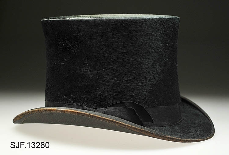 Flosshatt trukket med en filt av beverhår. Den er har en høy sylindrisk pull og en smal oppbrettet brem. Det er festet et svart hattebånd (sløyfe) på pullen. På toppen av pullen er det et lite hull, cirka 0, 8 cm i diameter. Hullet er dekket med en finmasket netting.  Trolig fungerer dette hullet som en slags lufting for den som bærer hatten.  Hatten bærer noe preg av slitasje, men sett i forhold til at den er over 110 år gammel er den i fint skikk. Svettebåndet inni hatten er løst. Inni hatten er varemerket plassert like ved luftehullet.  I og med at svettebåndet har løsnet, så avdekker det påtegninger med blyant som har ligget skjult under dette båndet. Kanskje er dette notater som er gjort under produksjon av hatten (registrator er usikker ). 