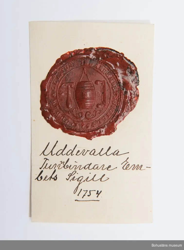 Föremålet visas i basutställningen Uddevalla genom tiderna, Bohusläns museum, Uddevalla.

Uddevalla tunnbindareämbetes sigill 1754 i rött sigillack, uppklistrat på en vit kartongbit med handskrivna texten:
Uddevalla 
Tunnbindare
Em-
bets Sigill 
1754

På sigillet avbildat en tunna, ett bandjärn och en däxel.
Sigillet är 4 cm diam.

Tillverkningstid avser sigillstampen som bör vara gjord då eller möjligen senare. Själva sigillet kan vara tillverkat senare.