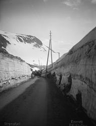En bil på veg mellom høye brøytekanter på Strynsfjellet.