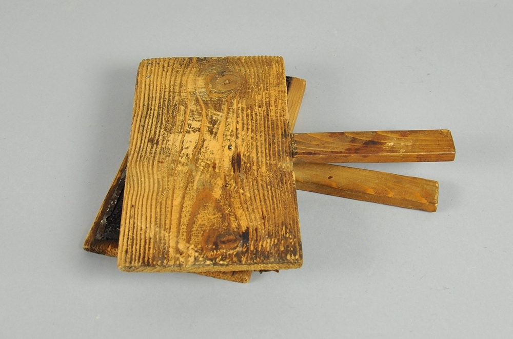 To treplater hvor innsiden av begge platene er dekket av  en skinnduk med tettsittende nåler. Begge treplatene har håndtak.