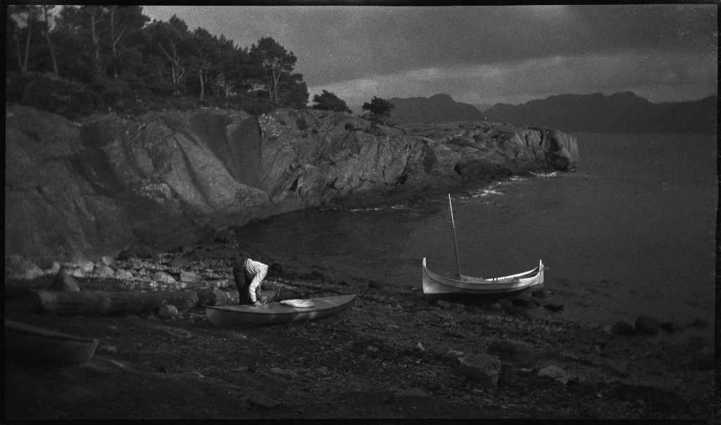 Fire unge menn på tur med nordlandsbåten og kajakker til Idse, ved innseilingen til Høgsfjorden. De har satt opp to telt og slapper av med blant annet kikkert og å stå på hendene. På bilde 14 er de ute med seil på nordlandsbåten.