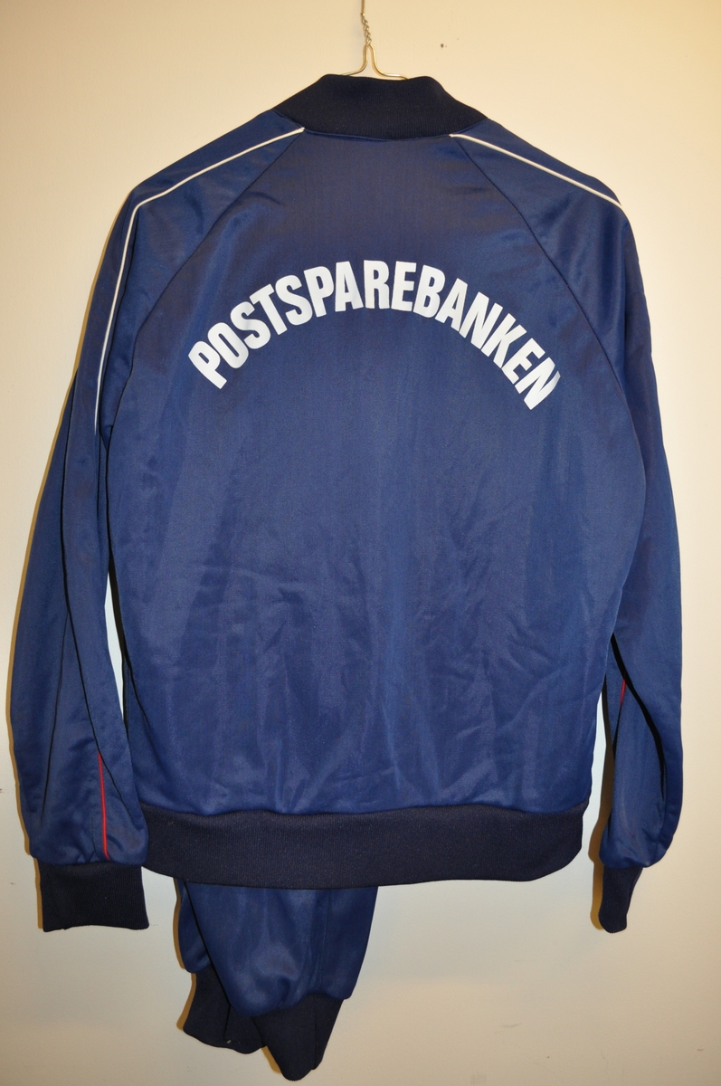 Treningsdress (bukse og jakke) med Postbankens logo og ordet "Sportsmann", samt ordet "Postsparebanken" på ryggen. Jakken har to stikklommer.  Størrelse 48.