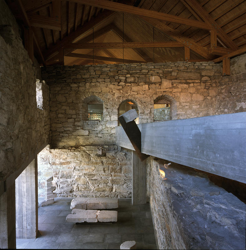 Ramper i rå betong går gjennom den tidligere låven for å løfte publikum opp fra de skjøre middelalderruinene.