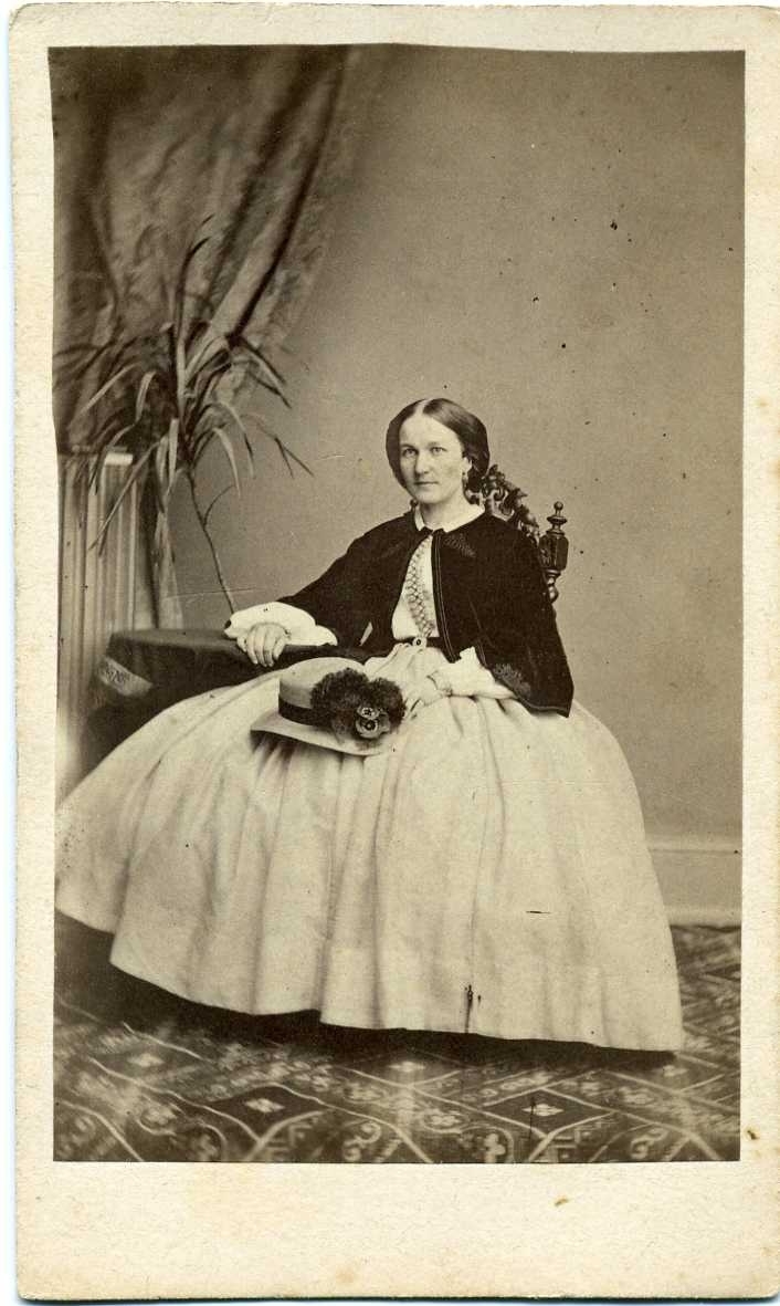 Kabinettsfotografi: Fröken Rydell, Gränna. Sittande på en stol i vid ljus kjol med en hatt vilande på knät.
