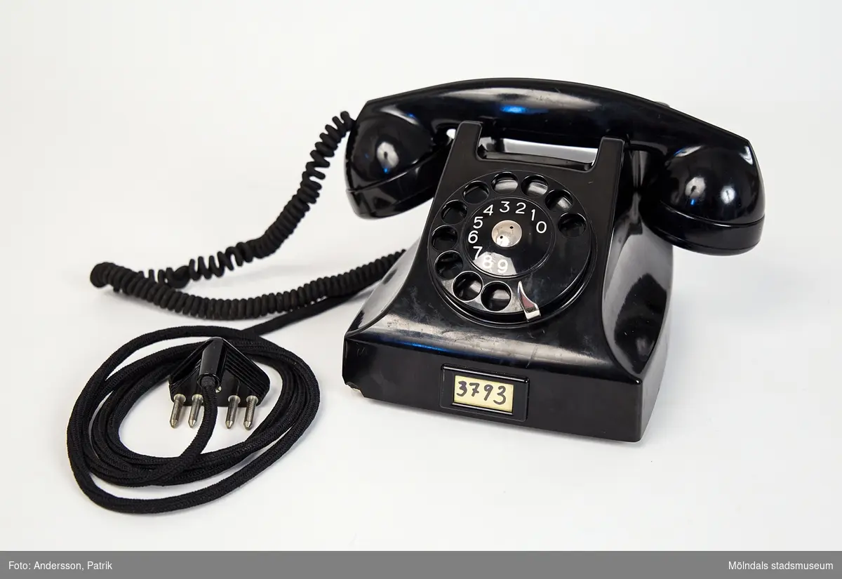Svart telefon.Denna telefon har använts i givarens föräldrahem i Kållered från 1950-talet och till 1970-talet  (troligtvis). Telefonen stod på en liten telefonhylla av teak, under hyllan låg telefonkatalogen, den blå med tre kronor på framsidan.