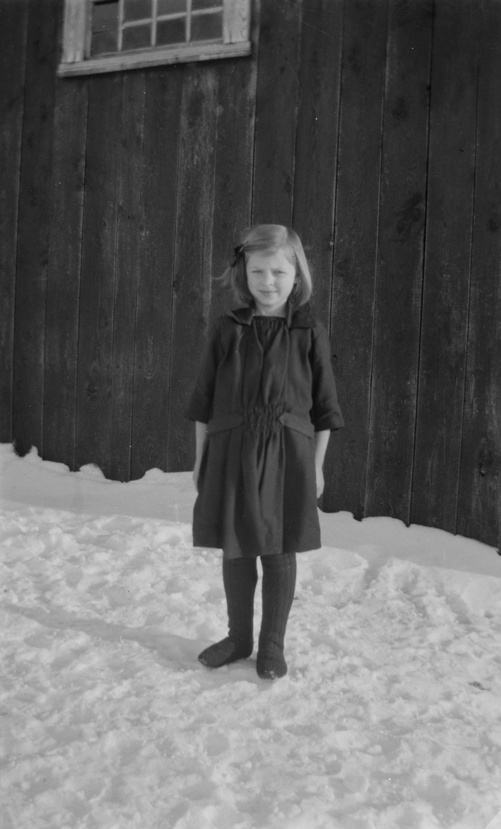 Jente står foran husvegg i snøen.