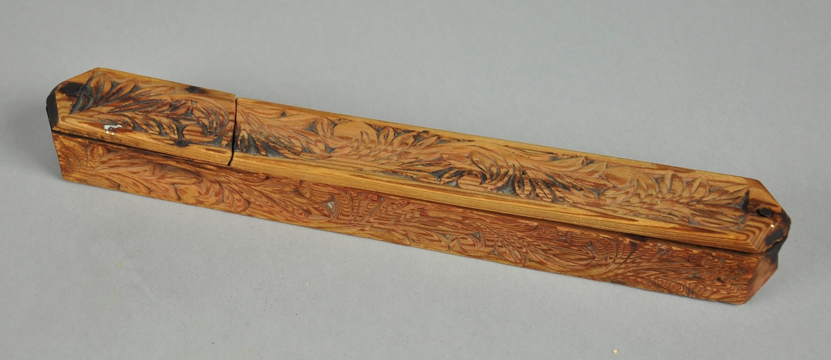 Pennal av tre med akantusutskjæringer på tre sider. Pennalet har et lokk som kan skyves til siden og er festet med en spiker.