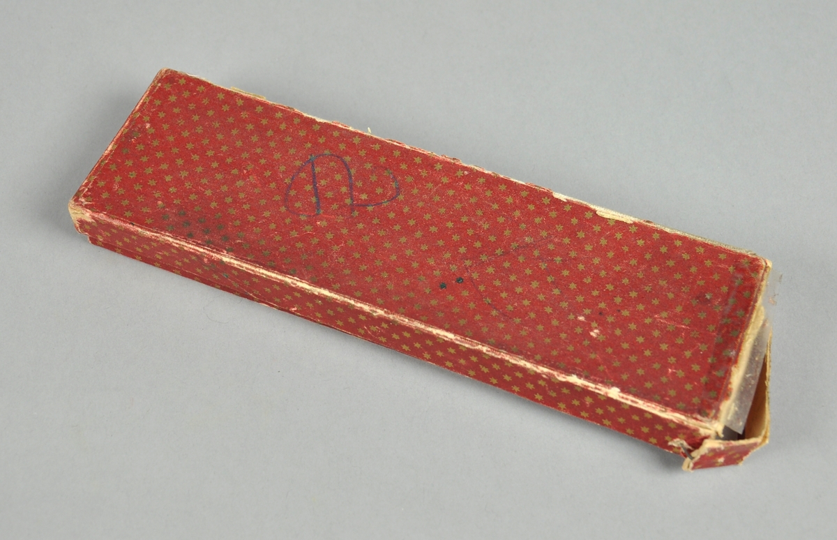 Eske av kartong som er kledd med rødt papir med gullstjerner. I esken er det noen blyanter, penneskaft og en pennestift.