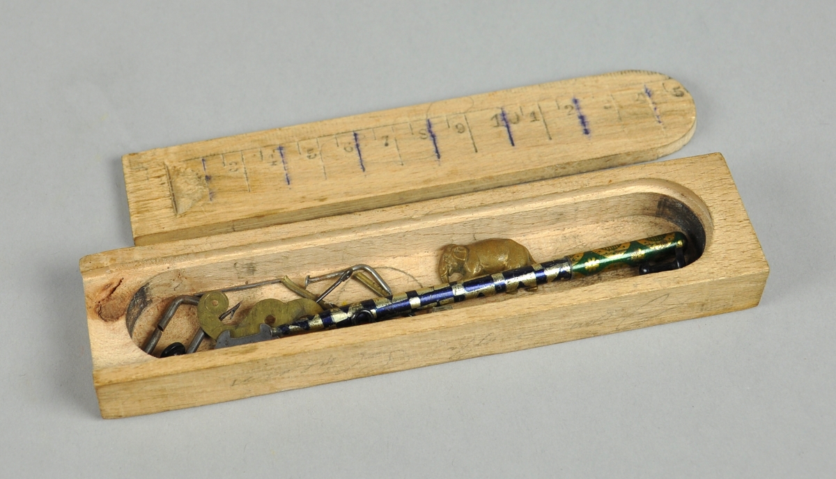 Pennal av tre med skyvelokk. I pennalet ligger det mange småting, som fiskekroker, nåler. hemper etc. På lokket er det risset inn en linjal