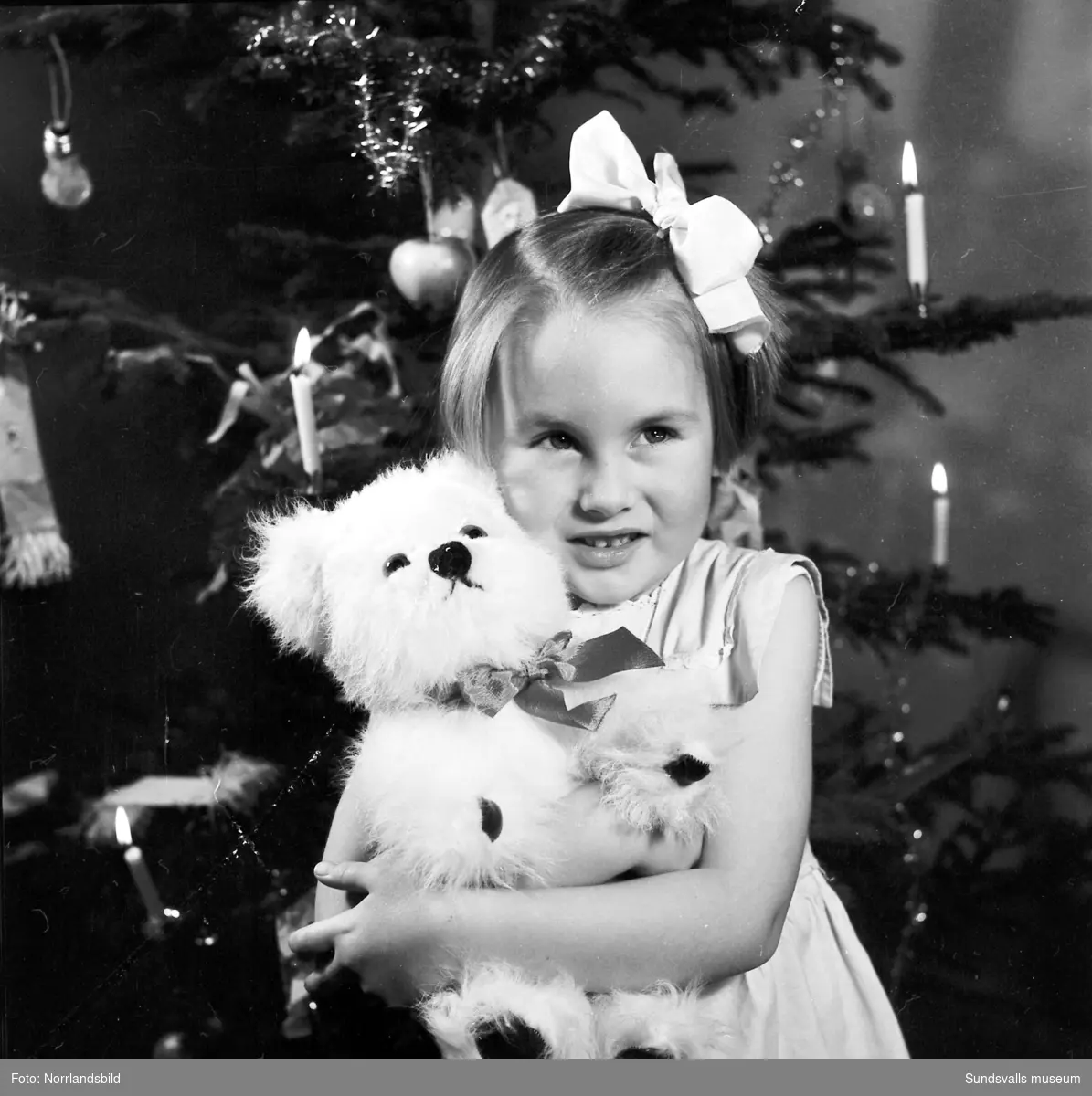 En liten flicka, Lena Tranberg, sitter framför julgranen med en nyöppnad present - en leksakshund.