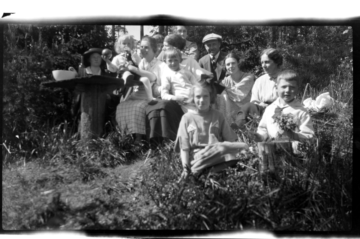 Alfhild Ferslew, Rolf Sundt jr., Hilda Sundt, Rolf Sundt sr., Anna Ferslew, Julie (Lillemor) Thaulow Aubert, Caspar Ferslew sitter sammen med ukjente mennesker på piknik i skogen. Fotografert 1922.