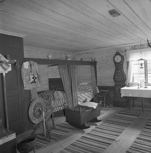 Köket i Sundmarsgården i Hamrånge Bergby
18 oktober 1982. Dubbla väggfasta sängar med omhängen, ett ståndur, en vagga, en spinnrock och långa trasmattor på trägolvet.