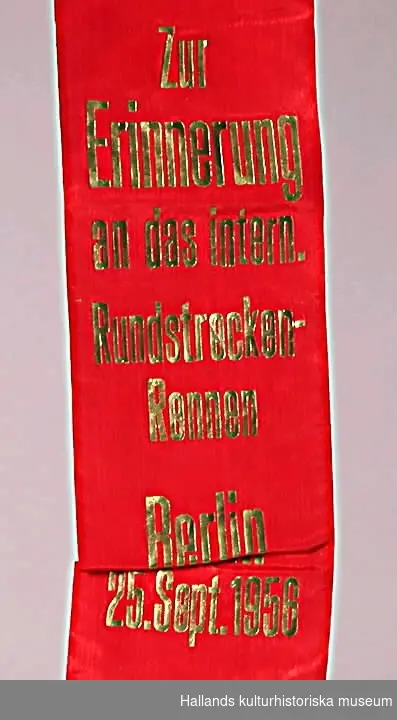 Röd vimpel av konstsiden med guldtext: "Zur Erinnerung an das intern. Rundstrecken-Rennen Berlin 25. Sept. 1956".