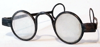 Glasögon med bågar av stål och runda glas. Skalmarna är avslutade med en ring på vardera sida.