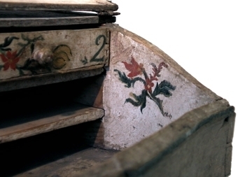 Blåmarmorerat skrivschatull med snedklaff som dekorerats med en medaljong med en skata i. Inuti är schatullet vitmålat och dekorerat med blommor och en basunängel. Fack för sex skjutlådor varav tre finns kvar, nummer 2, 4 och 6.
