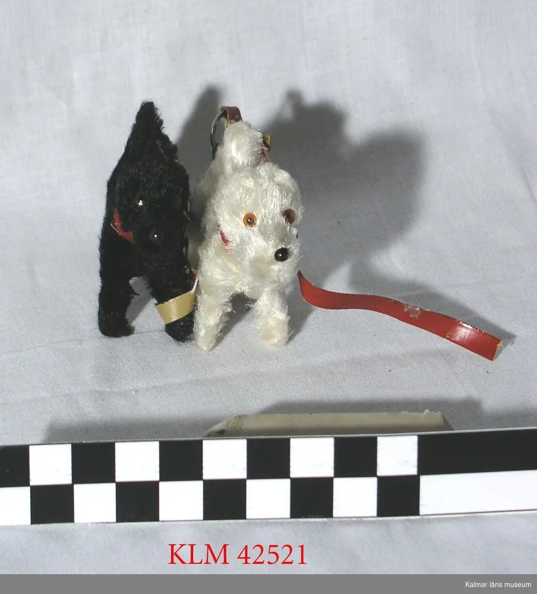 KLM 42521 Hund, leksak, 2 st, textil. Liten hund av konstpäls, blanka ögon och nos, rött koppel. En svart och en vit.