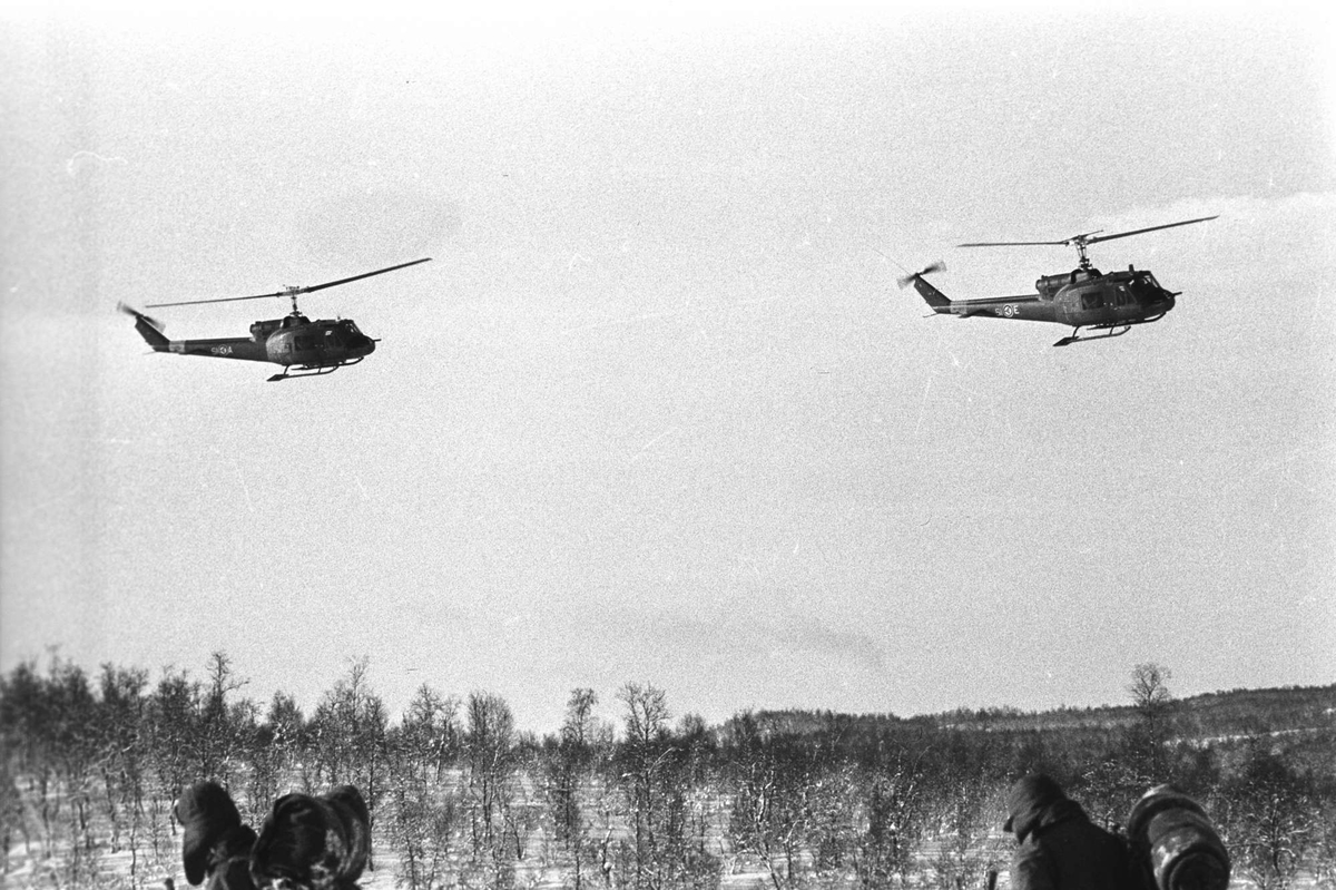 Helikoptre på øvelse ved Åsegarden. Hodene på to soldater i forgrunnen.