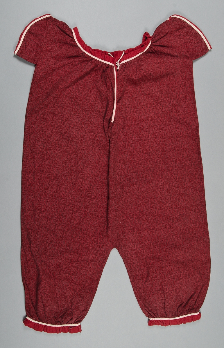 Baddräkt av röd kypertvävd bomullsflanell med svart tryckt mönster. Vita kantband. Runt ärmar, ringning och ben röd flanellkant.