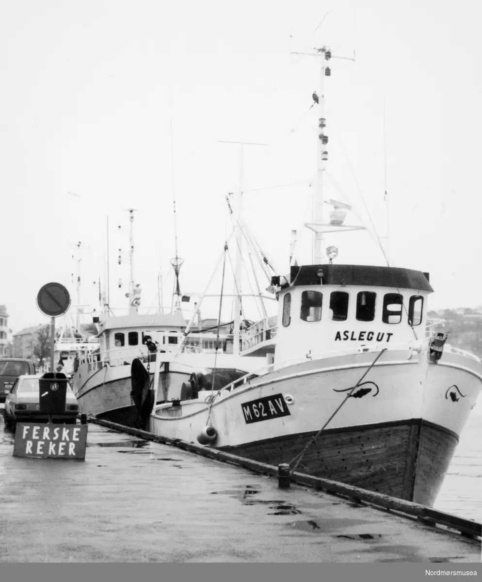 Pressefoto av fiskebåten "M-62-AV" Aslegut til kai ved Vågeveien/Vågekaia på Kirkelandet for å selge reker. Datering trolig mellom 1987-1990. Fotoarkivet stammer fra Nordmørsposten, og inngår nå i Nordmøre museums fotosamlinger.