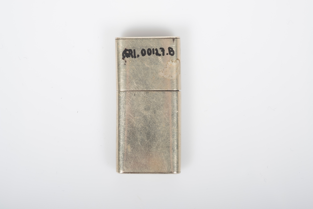 Fyrtøy i lysgul metall med inngravert fangenummer "7046" på lokket og navnet "Bell" på nederdelen.