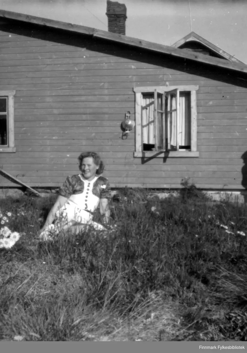 Gjertrud Hekkilæ fotografert en varm sommerdag, sittende i gresset foran et hus. Familiealbum tilhørende familien Klemetsen. Utlånt av Trygve Klemetsen. Periode: 1930-1960.