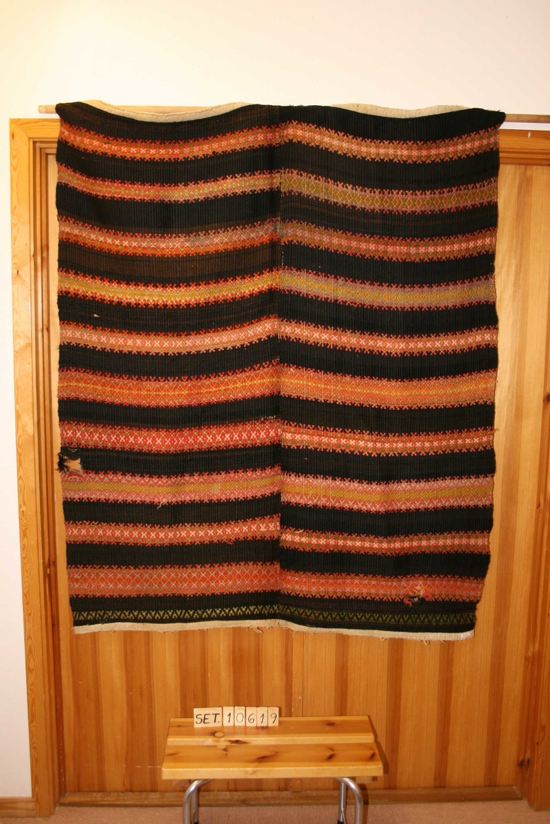 Rektangulært teppe med mønster, sydd saman av 2 breidder, falda og påsydd kanting i båe endar.