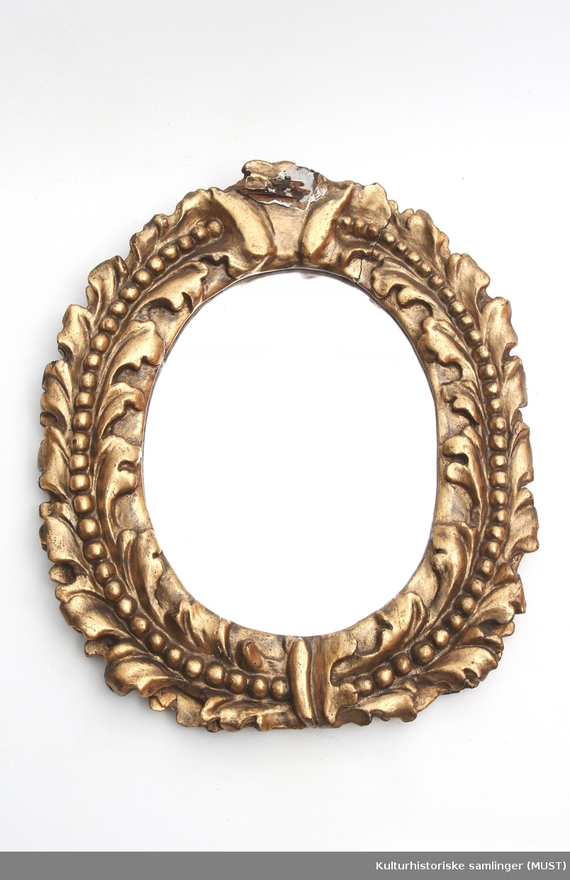 Ovalformet speil med med en enkel bladkrans rundt. I midten av denne går en perlerrad.