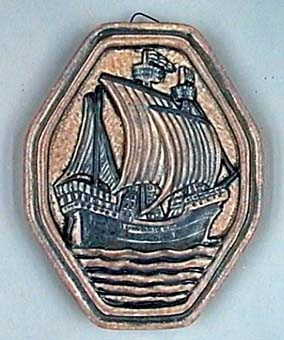 Handtagsplatta av porslin, formad som en oval, åttkantig form i reliefgjutning föreställande medeltida segelskepp från sidan, stiliserad i blått mot ljusbrun bakgrund.
