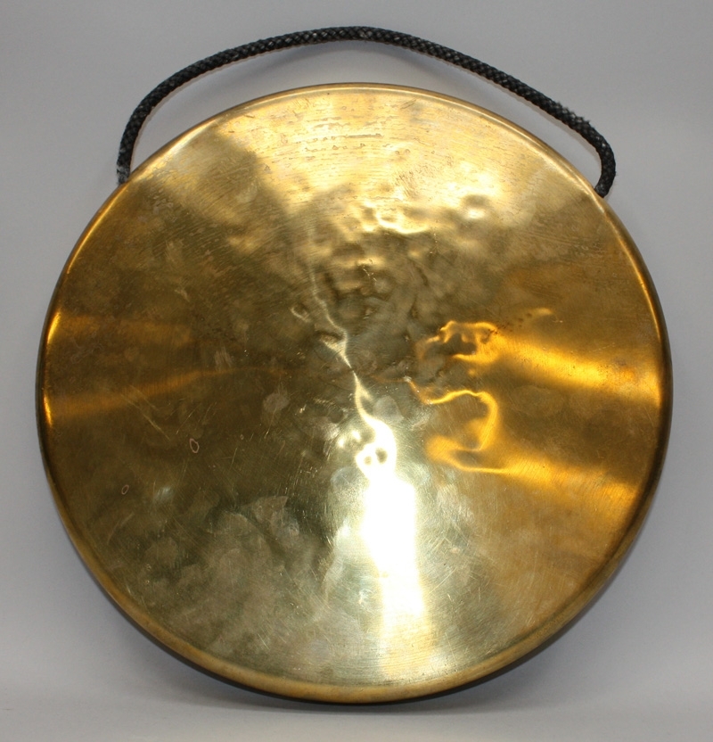 Gong-gong av mässing med snöre av flätat textilfiber som handtag. 

På baksidan sitter en svart klisterlapp med texten "100 % messing, Made in Denmark".