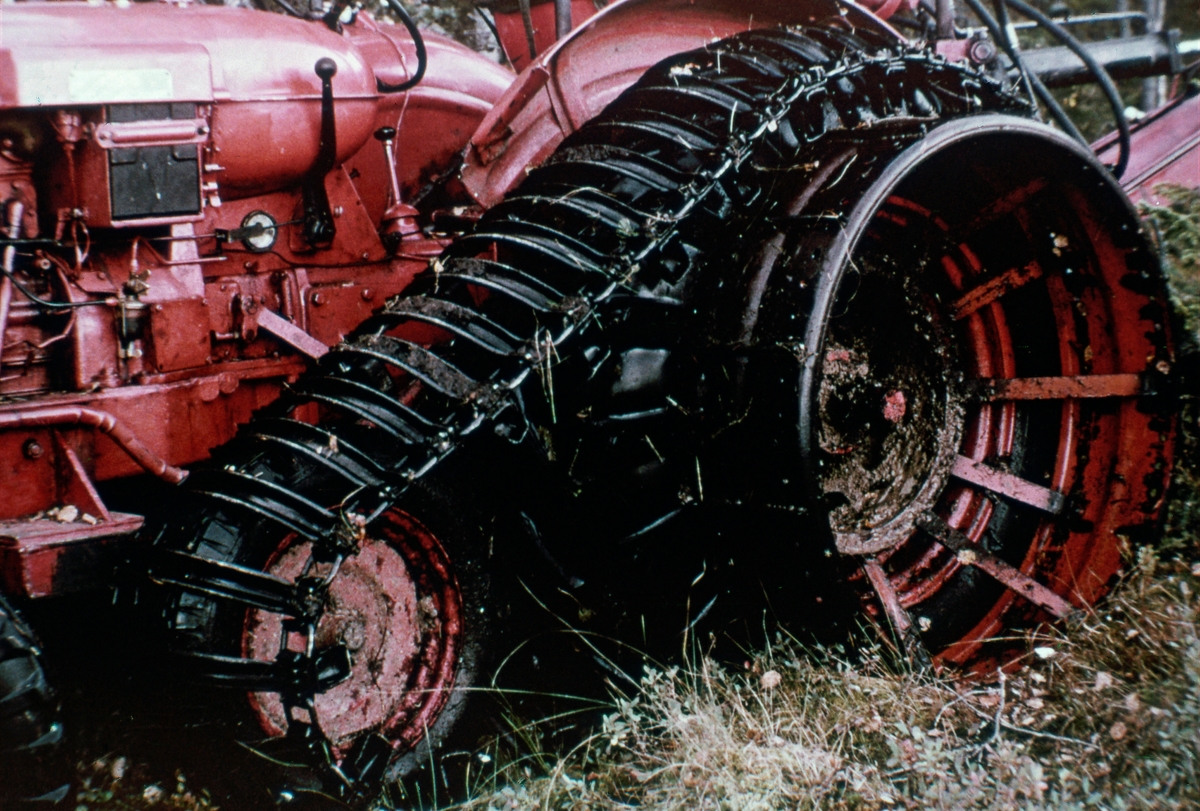 Detalj fra traktor som var påmontert hydraulisk gravemaskin med sikte på grøfting av fuktig, oksygenfattig myrtorv til produktiv skogsmark.  På fuktig myr var det fare for at traktorhjulene kunne grave seg ned i torva.  For å få kjøretøyet til å «flyte» på myra var den utstyrt med halvbelter og tvillinghjul av stål.

Dette er det tiende motivet i en bildeserie med tittelen «Skogreising på myr», produsert av Landbrukets film- og billedkontor i 1964.  Formålet med disse bildene var å stimulere til drenering av myrarealer med sikte på å forvandle dem til produktiv skogsmark.  I tekstheftet som fulgte med bildeserien skrev eksperten Ole Jerven følgende tekst til dette motivet: 

«Belter og bærehjul
For på minske marktrykket, er traktoren utstyrt med halvbelter.  I tillegg er det koblet på tvillinghjul (gummi el. jern).  På jernhjulene kan en – om nødvendig – feste plank og senke marktrykket ytterligere.  Med dette utstyret flyter maskinen bare "vatnet er litt grumset".»