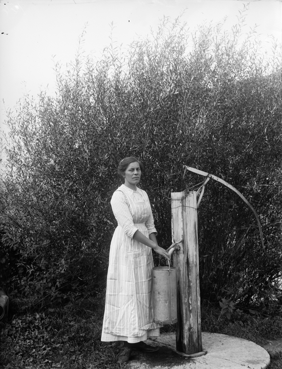 Hildegard Pettersson vid vattenpump på Alinders gård, Sävasta, Altuna socken, Uppland i början av 1900-talet