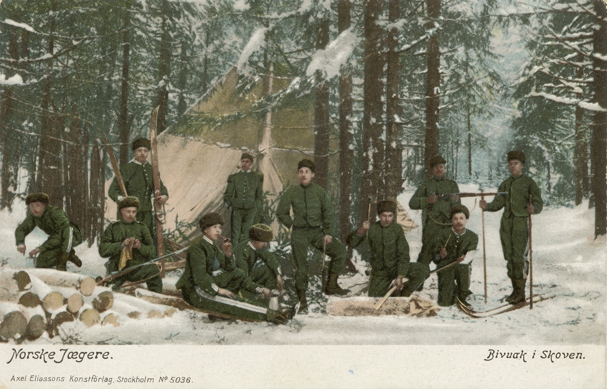 Postkort. Det håndkolorerte fotografiet på kortets fremside viser 11 uniformerte norske soldater i vinterskog. Motivbeskrivelse påtykt kortets fremside: "Norske jægere" og "Bivuak i skoven".
