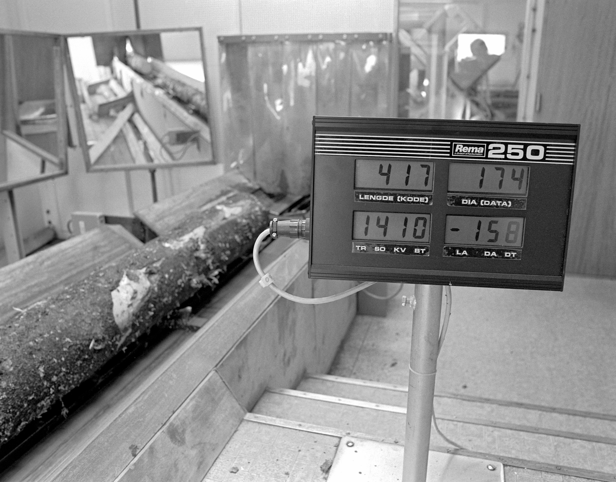 Automatisert tømmermåling ved Våler skurlag på Braskereidfoss i Solør, fotografert våren 1983, da denne teknologien var ny.  Tømmerstokkene gikk raskt gjennom målerhuset på et bånd.  Først passerte de ei ramme med en metallsøker, som skulle avsløre eventuelle metallsplinter, som kunne skape problmer i sagbruket.  Metall i tømmeret var et problem som var særlig vanlig i tømmerpartier som var avvirket i nærheten av det militære øvingsfeltet på Haslemoen i Våler.  Etter å ha passert metallsøkeren ble stokkene diametermålt ved passering av tre rammer (kryssmåling). Lengdemålinga ble gjort ved hjelp av fotoceller.  Under vegs ble stokkene besiktiget av tømmermålerne Rolf Sætre og Ola Strætkvern, som skulle besiktige tømmerstokkene og omklassifisere dersom de påviste feil som det automatiske måleranlegget ikke hadde registrert.    Målerne var særlig observante med hensyn til krok og gankvist.  Operatørene satt ved en terminal der de kunne lese av lengde- og diametermål, med og uten bark.  Maskinen hadde også en barktjukkelsestabell, samt kodesustemer for treslag, sortiment, kvalitet og barktjukkelse.  Våler skurlag mottok på dette tømmer med diamter ned til 10 centimeter (uten bark) for skurlastproduksjon.  Gjennom måleranlegget kunne det gå opptil 5 000 stokker i løpet av et arbeidsskift.  Etter å ha passert målerhuset ble stokkene ført videre på transportbåndet og vippet over i «lommer» for bestemte diameterklasser, vanligvis med intervaller på 2 centimeter.  Ved å mate sagbruket med store serier av tømmerstokker med samme dimensjon unngikk man hyppige omstillinger av sagbruksmaskineriet.